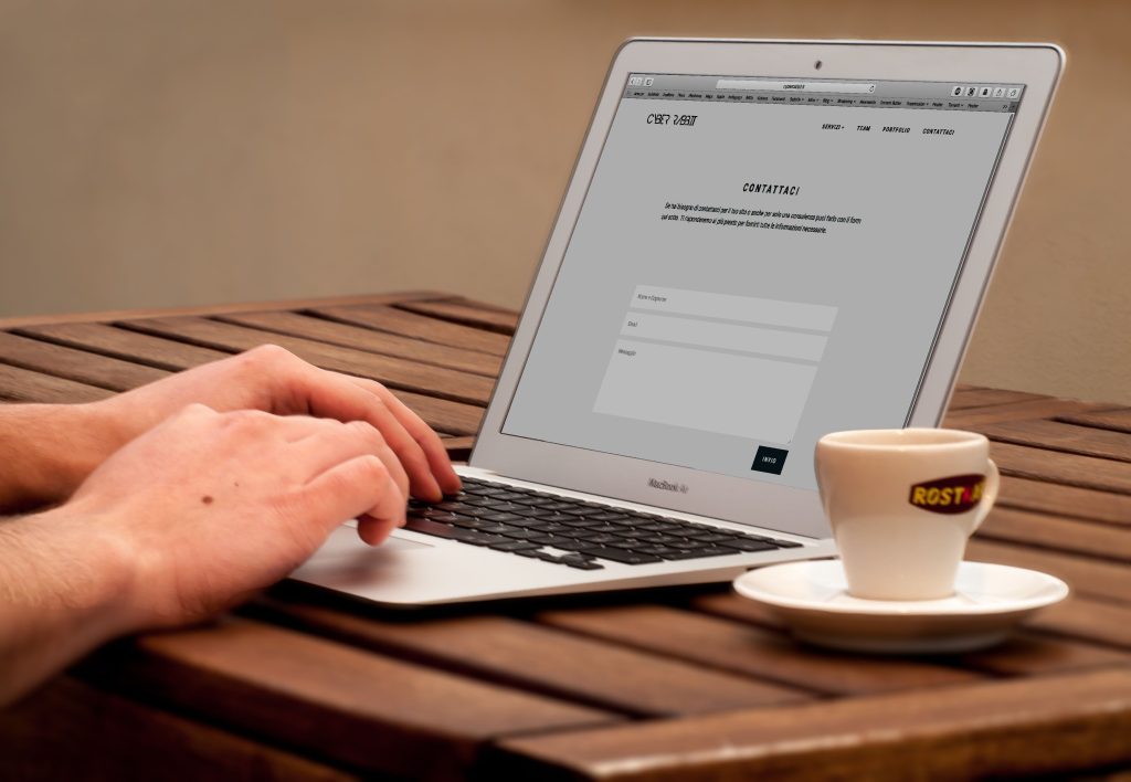 pexels photo 221043 221043 Close-up of hands typing on a laptop next to a cup of coffee on a wooden desk.
